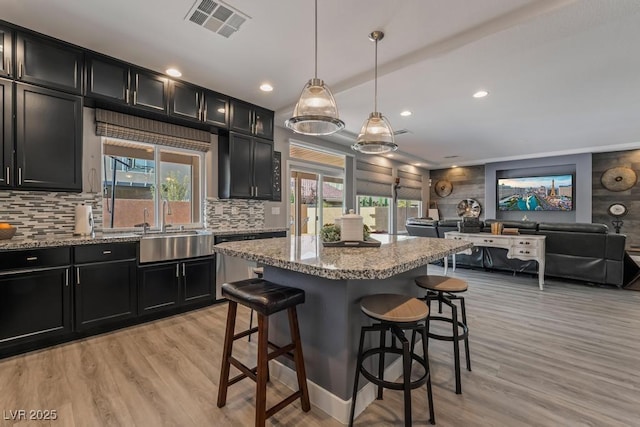 kitchen with a kitchen bar, hanging light fixtures, light hardwood / wood-style floors, and light stone counters