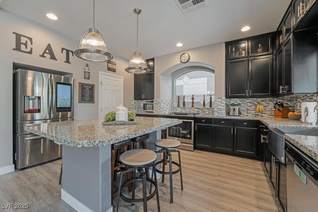 kitchen with stainless steel appliances, light wood-type flooring, pendant lighting, and a center island