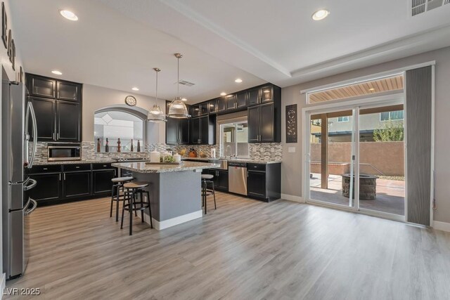 kitchen featuring light hardwood / wood-style flooring, a center island, decorative light fixtures, stainless steel appliances, and a breakfast bar