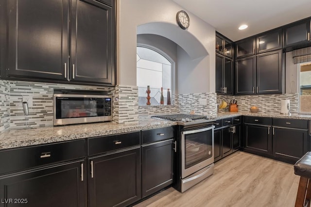 kitchen with appliances with stainless steel finishes, light hardwood / wood-style flooring, light stone counters, and decorative backsplash