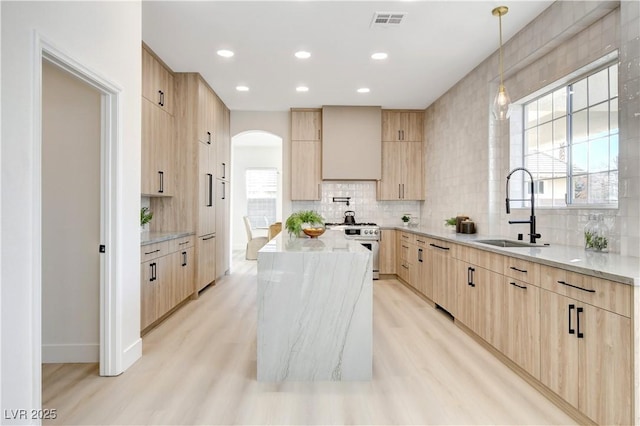 kitchen featuring a center island, high end stainless steel range oven, light brown cabinetry, light stone counters, and sink