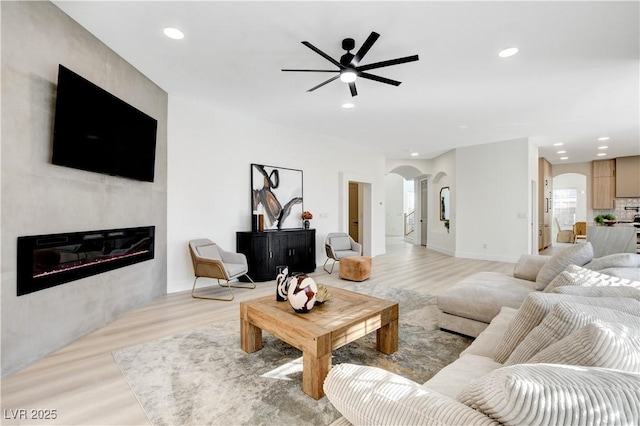 living room featuring a fireplace, ceiling fan, and light hardwood / wood-style floors