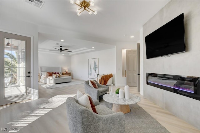 living room featuring a raised ceiling, ceiling fan, and light hardwood / wood-style floors