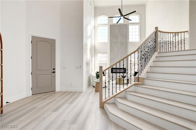 entryway with a towering ceiling, ceiling fan, and light wood-type flooring