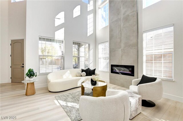 living room featuring a towering ceiling, light wood-type flooring, a wealth of natural light, and a fireplace