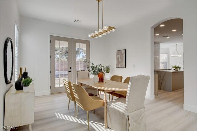 dining room featuring a notable chandelier, french doors, light hardwood / wood-style floors, and a healthy amount of sunlight