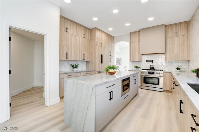 kitchen with light stone counters, premium range hood, light hardwood / wood-style flooring, a center island, and stainless steel appliances