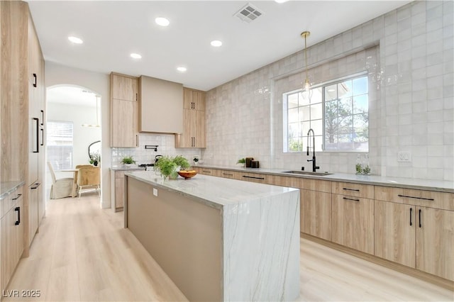 kitchen featuring light stone countertops, light brown cabinetry, a kitchen island, sink, and light hardwood / wood-style flooring