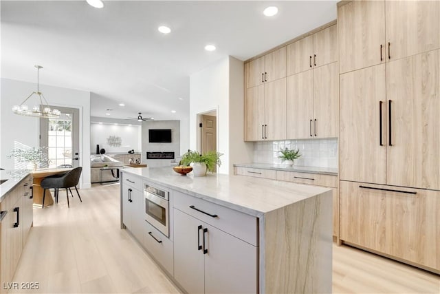 kitchen featuring a center island, light stone counters, light brown cabinets, light hardwood / wood-style floors, and backsplash