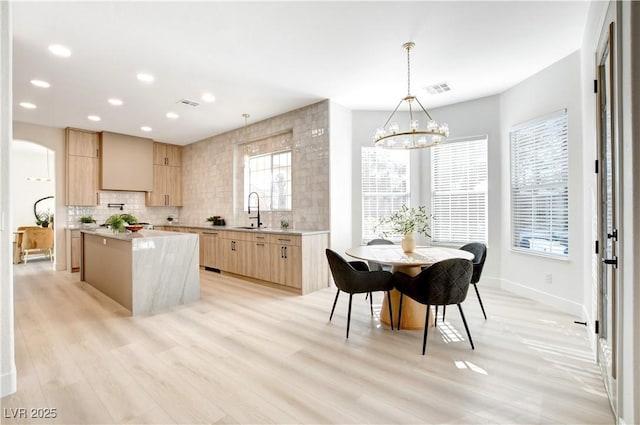 kitchen featuring light hardwood / wood-style flooring, pendant lighting, light brown cabinetry, a notable chandelier, and a kitchen island