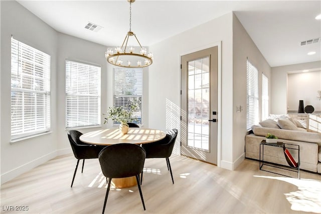 dining room with light hardwood / wood-style floors, a healthy amount of sunlight, and a notable chandelier