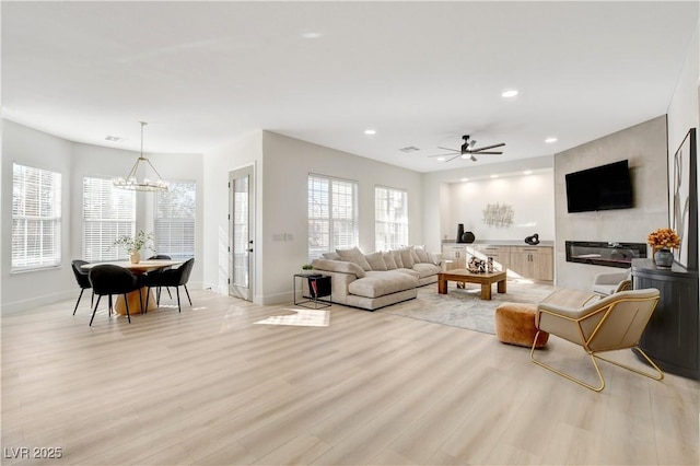 living room with light hardwood / wood-style floors, a wealth of natural light, and ceiling fan with notable chandelier