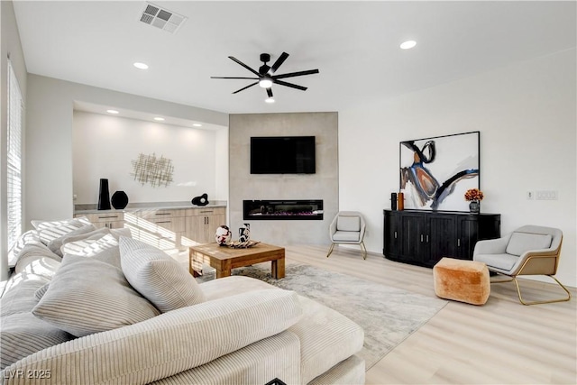 living room featuring ceiling fan, light wood-type flooring, and a fireplace