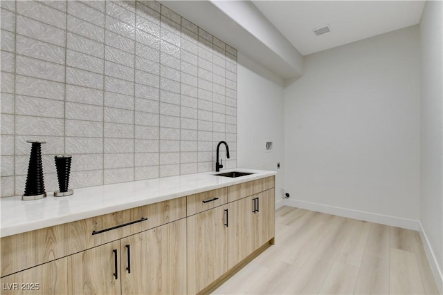 kitchen with sink, light hardwood / wood-style floors, light brown cabinetry, and backsplash