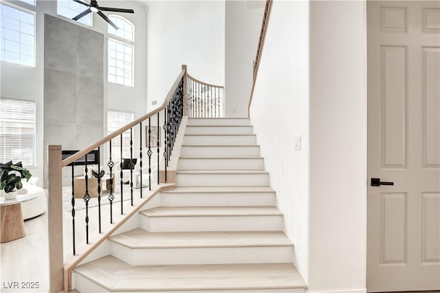 stairway featuring a towering ceiling, ceiling fan, and a healthy amount of sunlight