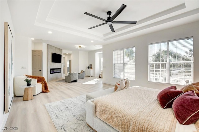 bedroom featuring light hardwood / wood-style floors, ceiling fan, a tray ceiling, and a large fireplace