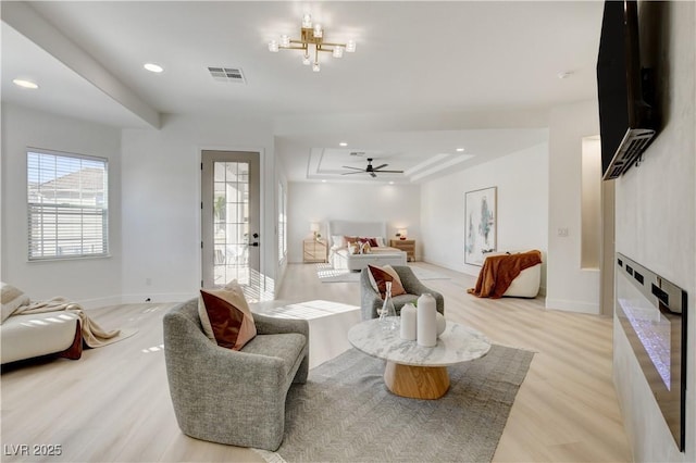 bedroom featuring a raised ceiling, access to exterior, multiple windows, and light hardwood / wood-style flooring