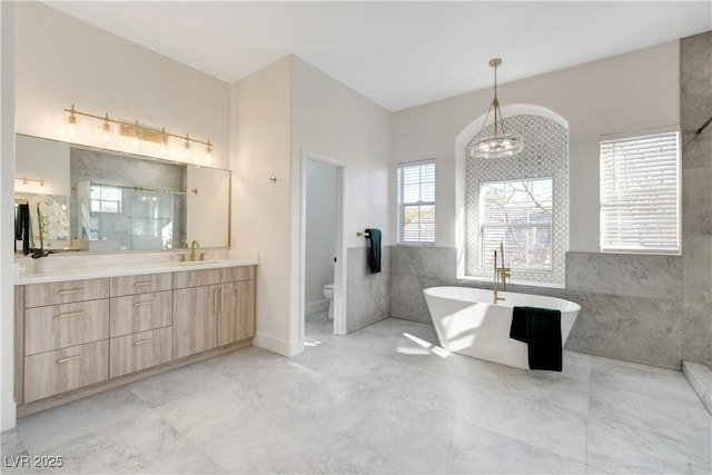 full bathroom featuring tile walls, toilet, independent shower and bath, vanity, and a notable chandelier