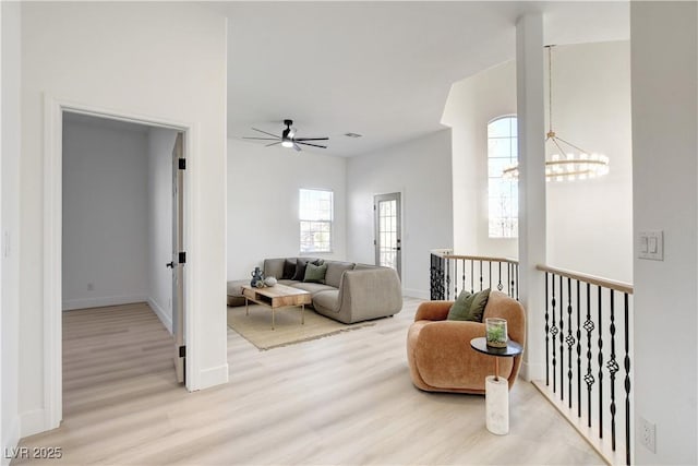 living area featuring ceiling fan with notable chandelier, light wood-type flooring, and a healthy amount of sunlight