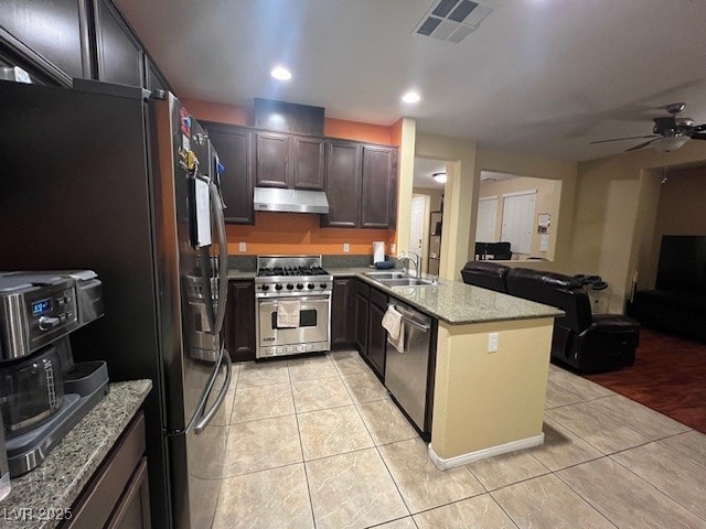 kitchen featuring appliances with stainless steel finishes, light stone countertops, kitchen peninsula, light tile patterned floors, and sink