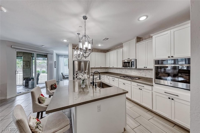 kitchen with white cabinets, appliances with stainless steel finishes, hanging light fixtures, an island with sink, and sink