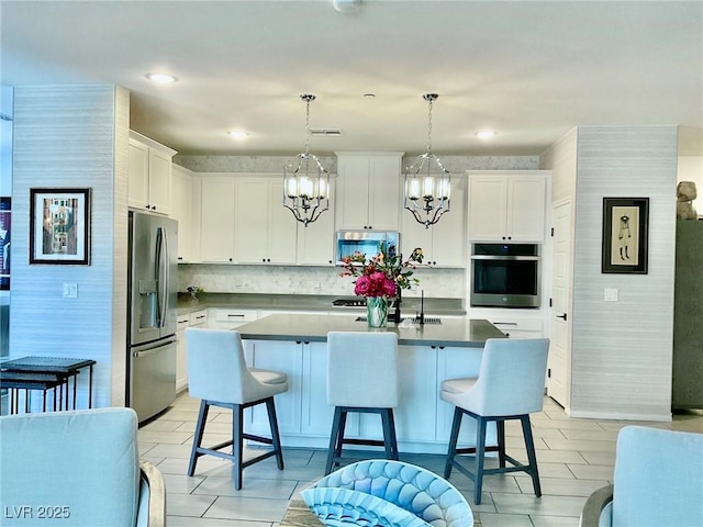 kitchen featuring pendant lighting, stainless steel appliances, tasteful backsplash, a kitchen island with sink, and white cabinetry