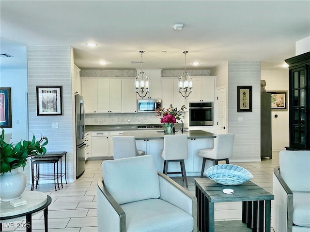 kitchen featuring white cabinetry, an island with sink, backsplash, pendant lighting, and appliances with stainless steel finishes