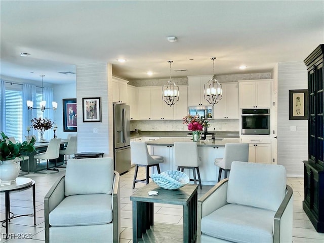 kitchen with stainless steel appliances, decorative light fixtures, white cabinetry, an island with sink, and decorative backsplash