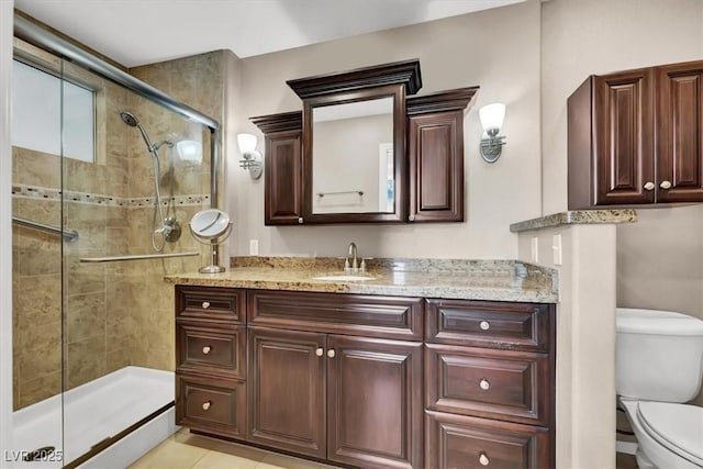 bathroom with toilet, vanity, tile patterned flooring, and tiled shower