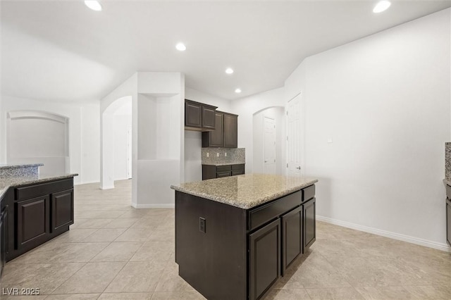 kitchen featuring a center island, light tile patterned floors, light stone counters, decorative backsplash, and dark brown cabinets