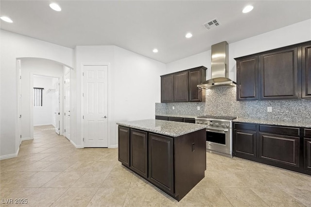 kitchen featuring light stone counters, wall chimney exhaust hood, a center island, high end range, and dark brown cabinets