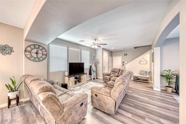 living room featuring ceiling fan, light hardwood / wood-style floors, and a textured ceiling