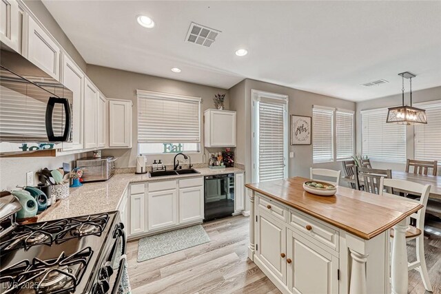 kitchen with pendant lighting, a center island, black appliances, white cabinetry, and sink