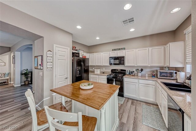 kitchen with light stone countertops, black appliances, light wood-type flooring, white cabinets, and sink