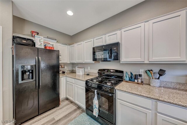 kitchen with light stone countertops, light hardwood / wood-style floors, black appliances, and white cabinetry