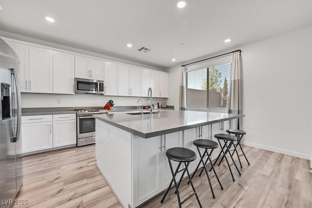 kitchen featuring light hardwood / wood-style floors, a center island with sink, sink, stainless steel appliances, and white cabinets