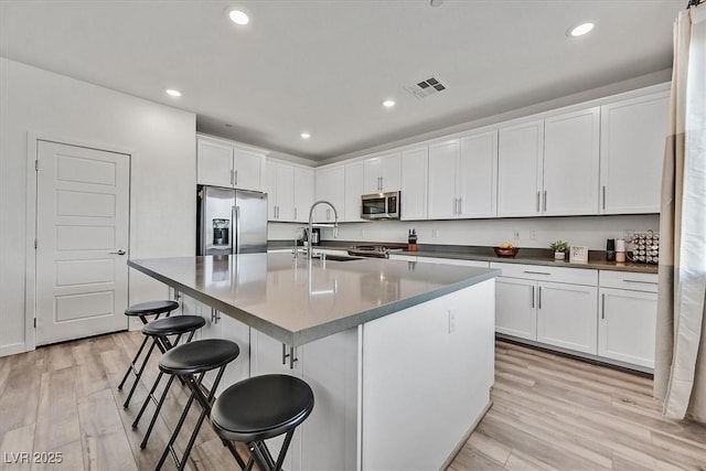 kitchen featuring stainless steel appliances, light wood-type flooring, an island with sink, sink, and white cabinetry