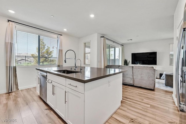 kitchen with sink, stainless steel appliances, white cabinets, light hardwood / wood-style flooring, and a kitchen island with sink