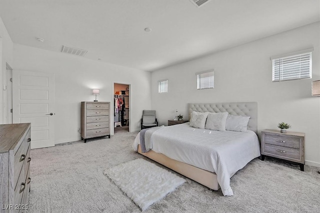 bedroom featuring a walk in closet, a closet, multiple windows, and light colored carpet