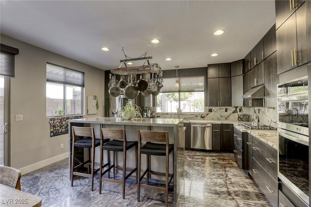 kitchen with appliances with stainless steel finishes, hanging light fixtures, a breakfast bar, dark brown cabinetry, and backsplash