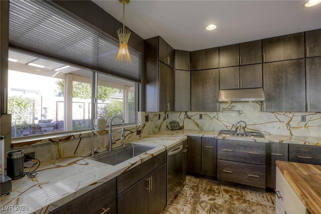 kitchen featuring stainless steel appliances, light stone counters, dark brown cabinetry, sink, and decorative light fixtures