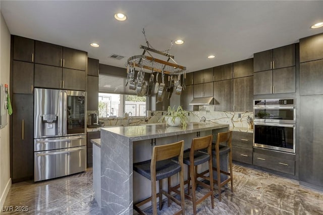 kitchen with a kitchen breakfast bar, decorative backsplash, dark brown cabinetry, a kitchen island, and appliances with stainless steel finishes