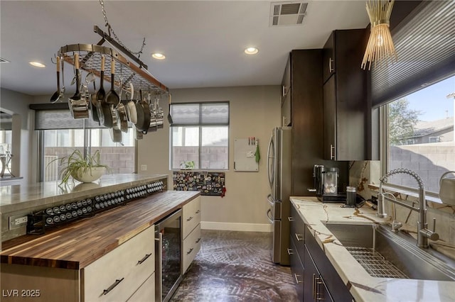 kitchen featuring beverage cooler, stainless steel fridge, wood counters, and sink