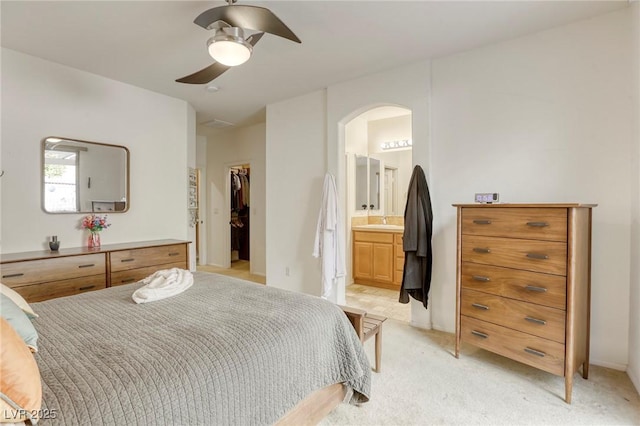 bedroom with a closet, light carpet, ceiling fan, a spacious closet, and ensuite bathroom