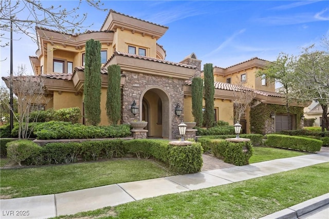 mediterranean / spanish house featuring stone siding, a front lawn, a tile roof, and stucco siding