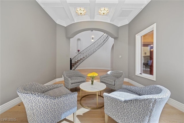 living area with arched walkways, coffered ceiling, beamed ceiling, baseboards, and stairs