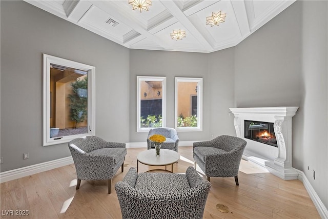 living area with light wood-type flooring, baseboards, coffered ceiling, and a glass covered fireplace