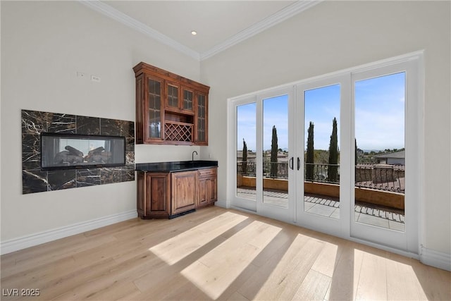 interior space featuring baseboards, ornamental molding, indoor wet bar, and light wood-style floors