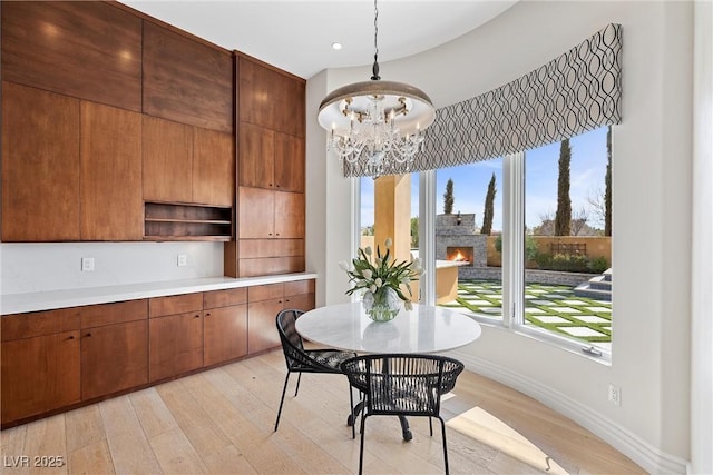 dining room with recessed lighting, a warm lit fireplace, light wood finished floors, and an inviting chandelier