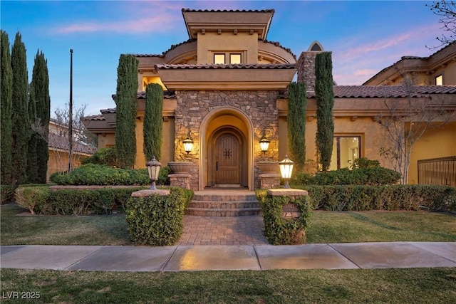 mediterranean / spanish house with stone siding, a front yard, and stucco siding